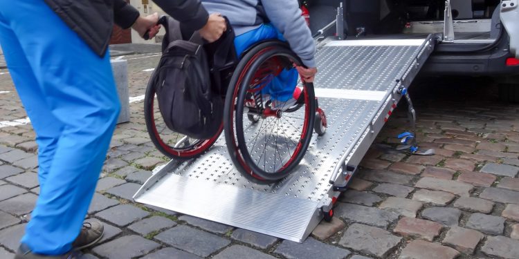 Assistant helping disabled person on wheelchair with transport using accessible van ramp