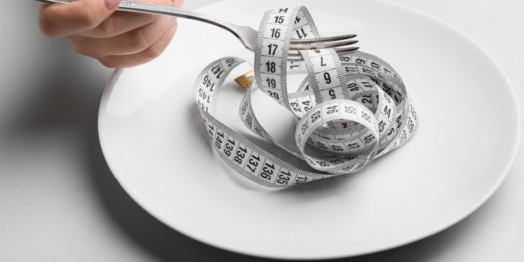 Female hand with plate, fork and measuring tape on grey background. Concept of anorexia