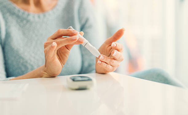 Mature woman doing blood sugar test at home in a living room. Selective focus to her finger.